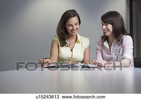 Two women reading papers at desk View Large Photo Image Stock Image - Two women reading papers at desk. Fotosearch