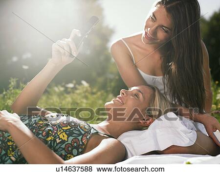 Two women sitting in meadow using mobile phone View Large Photo Image Stock Photo - Two women sitting in meadow using mobile phone. Fotosearch