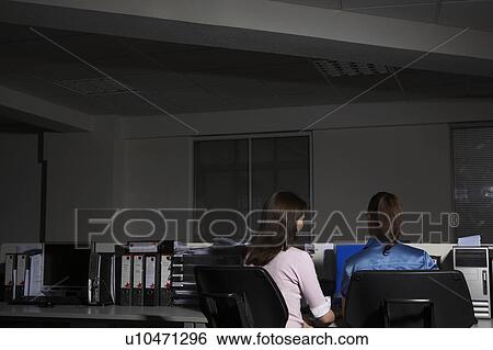 Stock Photograph - Two women sitting in office, back view. Fotosearch