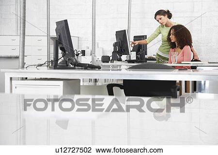 Two young women at desk, one pointing at computer monitor View Large Photo Image Stock Image - Two young women at desk, one pointing at computer monitor. Fotosearch