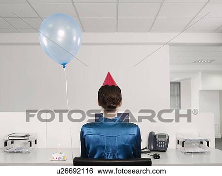 Stock Photograph - Woman celebrating birthday, working alone in office. Fotosearch