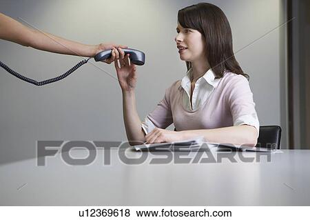 Woman handing over phone receiver to colleague at desk View Large Photo Image Stock Photo - Woman handing over phone receiver to colleague at desk. Fotosearch