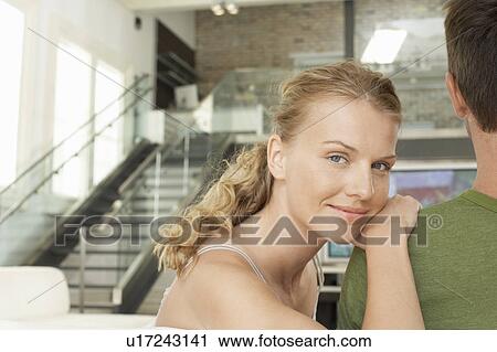 Stock Image - Woman leaning on man in modern apartment, portrait. Fotosearch