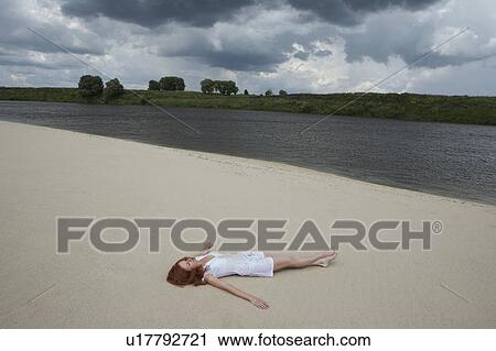 Stock Image - Woman Lying on Beach Along River. Fotosearch