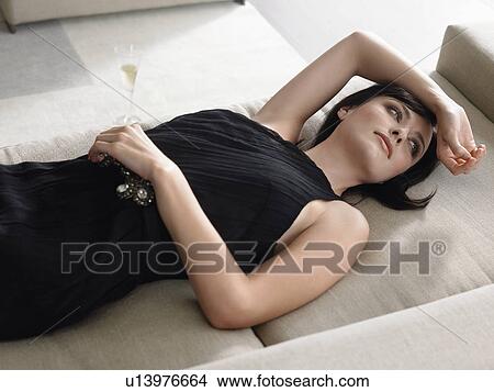 Picture - Woman lying on couch holding champagne glass in living room. Fotosearch