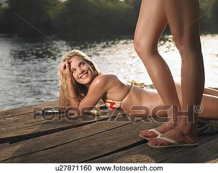 Stock Image - Woman lying on jetty looking up at second woman. Fotosearch