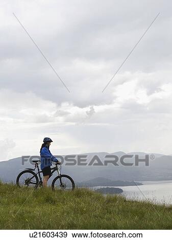 Stock Photo - Woman on bicycle near lake. Fotosearch