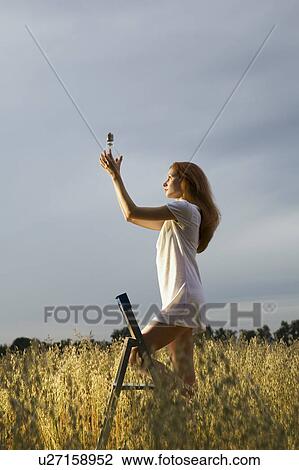 Stock Image - Woman Raising Large Light Bulb Toward the Sun. Fotosearch