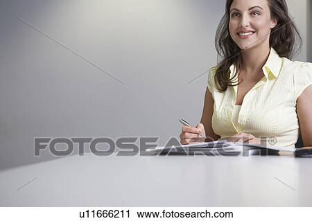 Stock Image - Woman sitting at desk and writing. Fotosearch