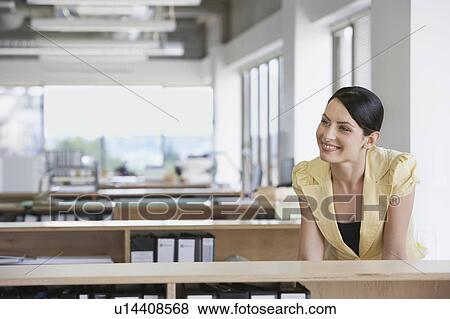 Woman sitting at desk in office, smiling View Large Photo Image Stock Photo - Woman sitting at desk in office, smiling. Fotosearch