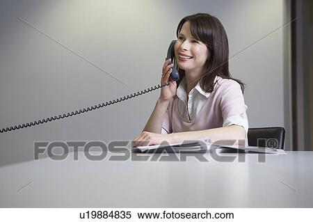 Stock Photography - Woman sitting at desk, talking on phone. Fotosearch