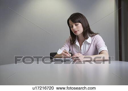 Woman sitting behind desk, writing notes View Large Photo Image Stock Image - Woman sitting behind desk, writing notes. Fotosearch