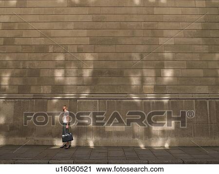 Stock Image - Woman standing by wall. Fotosearch