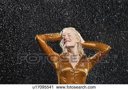 Stock Image - Woman Standing in Rain, arms raised, letting raindrops fall on face. Fotosearch