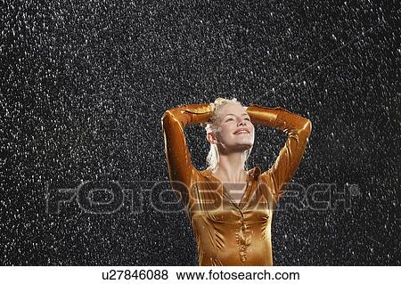 Stock Photo - Woman Standing in Rain, arms raised, letting raindrops fall on face. Fotosearch