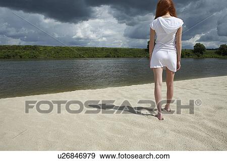 Stock Photo - Woman Standing on Beach Along River. Fotosearch