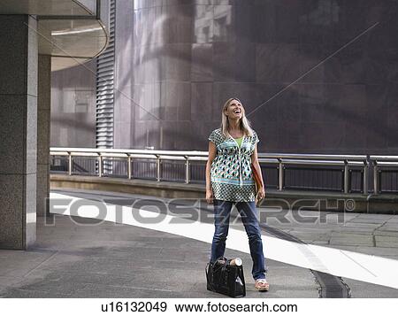 Stock Photo - Woman standing on sidewalk, looking up. Fotosearch