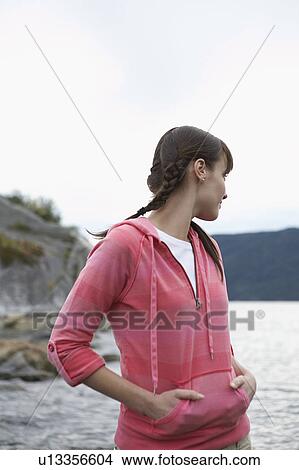 Picture - Woman with hands in pockets, standing by ocean. Fotosearch