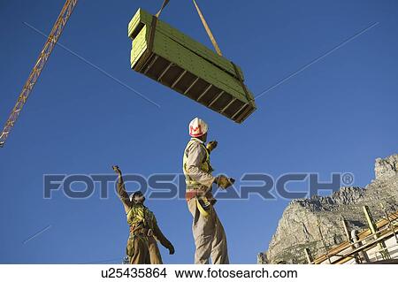 Picture - Workmen manoeuvre building materials on tower crane. Fotosearch