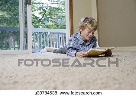 Young boy (5-6) lying on carpet reading book View Large Photo Image Stock Photo - Young boy (5-6) lying on carpet reading book. Fotosearch