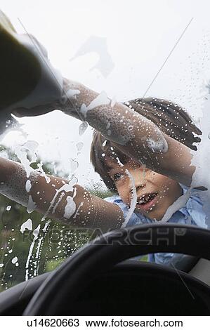 Stock Image - Young boy (7-9) washing car with sponge, view from inside car. Fotosearch
