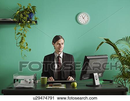 Young business man using computer at desk in office View Large Photo Image Stock Image - Young business man using computer at desk in office. Fotosearch
