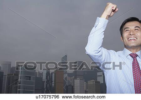 Young business man with raised arm, office buildings in background View Large Photo Image Stock Photograph - Young business man with raised arm, office buildings in background. Fotosearch