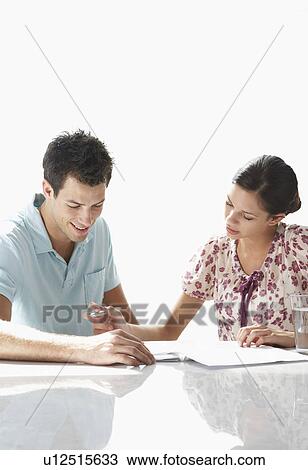 Young couple sitting at table, looking at sheets of paper View Large Photo Image Stock Image - Young couple sitting at table, looking at sheets of paper. Fotosearch