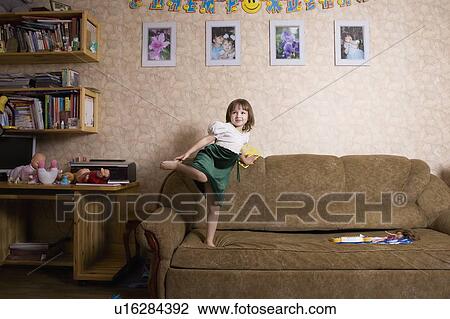 Stock Image - Young girl jumps on sofa. Fotosearch