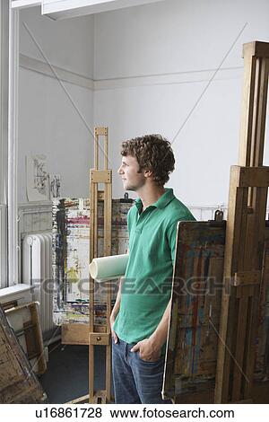 Young male artist looking out of the window in art studio View Large Photo Image Stock Photo - Young male artist looking out of the window in art studio. Fotosearch