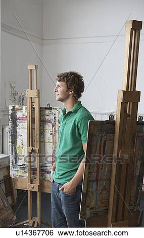 Stock Photograph - Young male artist looking out of the window in art studio. Fotosearch