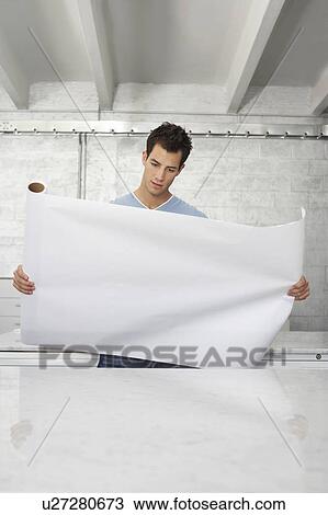 Young man holding and looking at big sheet of paper View Large Photo Image Stock Image - Young man holding and looking at big sheet of paper. Fotosearch