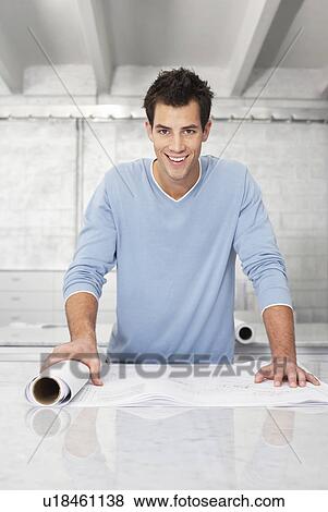Young man leaning on table, holding roll of paper View Large Photo Image Stock Photo - Young man leaning on table, holding roll of paper. Fotosearch