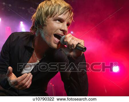 Stock Image - Young Man Singing into microphone on stage at Concert, low angle view. Fotosearch