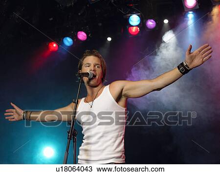 Young Man Singing into microphone on stage at Concert, low angle view View Large Photo Image Stock Image - Young Man Singing into microphone on stage at Concert, low angle view. Fotosearch
