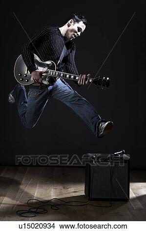 Picture - Young man with electric guitar jumping on stage. Fotosearch