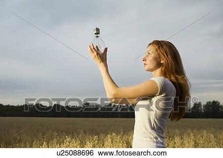 Stock Photograph - Young Woman in a Field Holding a Light Bulb. Fotosearch