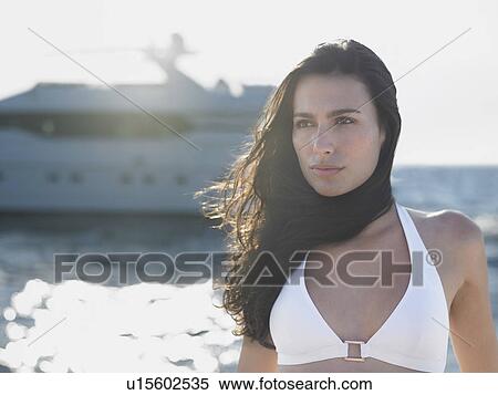Stock Photography - Young woman in bikini against sea with yacht in background. Fotosearch