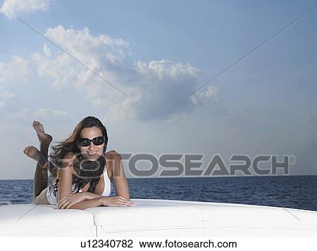 Stock Image - Young woman in bikini lying on cushions on yacht. Fotosearch