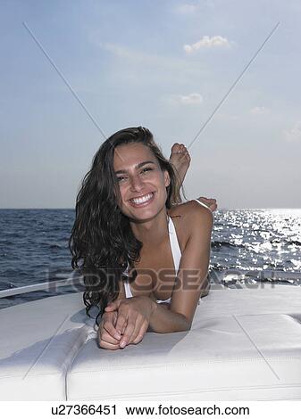 Stock Image - Young woman in bikini lying on cushions on yacht. Fotosearch