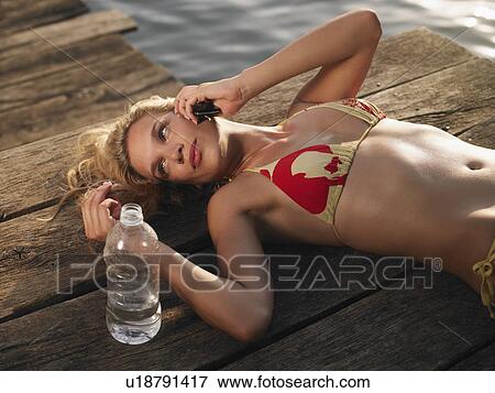 Young woman in bikini lying on jetty using mobile View Large Photo Image Stock Photo - Young woman in bikini lying on jetty using mobile. Fotosearch
