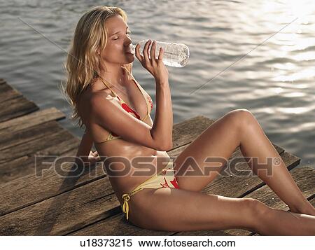 Young woman in bikini sitting on jetty drinking water View Large Photo Image Stock Photography - Young woman in bikini sitting on jetty drinking water. Fotosearch