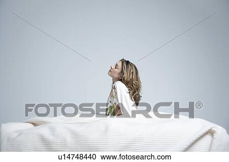 Stock Image - Young woman in dressing gown sitting in bed. Fotosearch