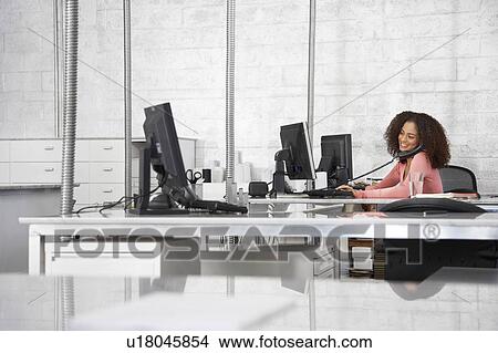 Young woman in office, using computer and phone, smiling View Large Photo Image Picture - Young woman in office, using computer and phone, smiling. Fotosearch