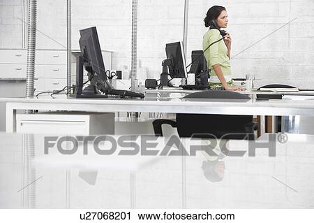 Stock Image - Young woman in office, using phone. Fotosearch
