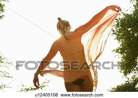 Young woman in swimsuit dancing with transparent robe in park, low angle view View Large Photo Image Stock Photo - Young woman in swimsuit dancing with transparent robe in park, low angle view. Fotosearch