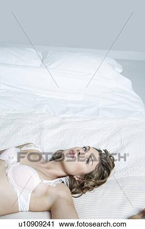 Stock Image - Young woman in underwear lying on bed, elevated view. Fotosearch