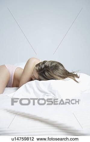 Stock Image - Young woman in underwear lying on bed, close-up. Fotosearch