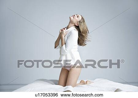 Stock Photograph - Young woman kneeling on bed, smiling. Fotosearch