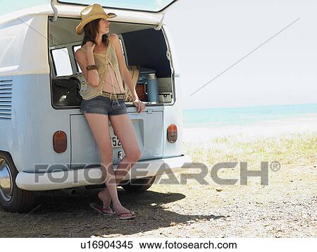 Stock Photography - Young woman leaning on open tailgate of camper van, parked by sea. Fotosearch